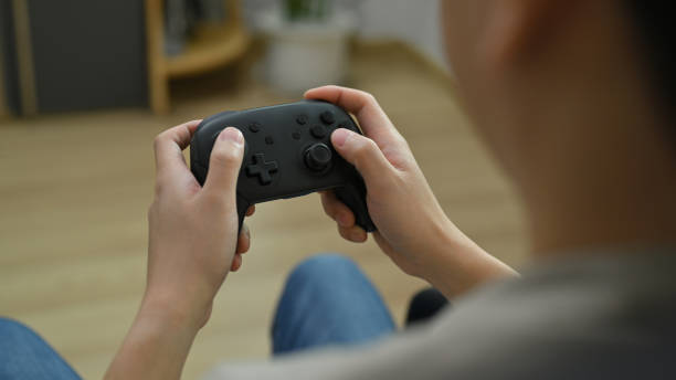 istock View over shoulder of young man holding wireless controller playing video game. Entertainment, technology and hobby concept. 1480503674