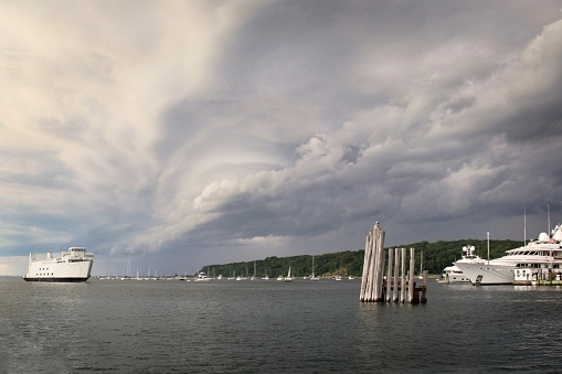 a yacht and marina with a ferry arriving in a bay with passing storm clouds above