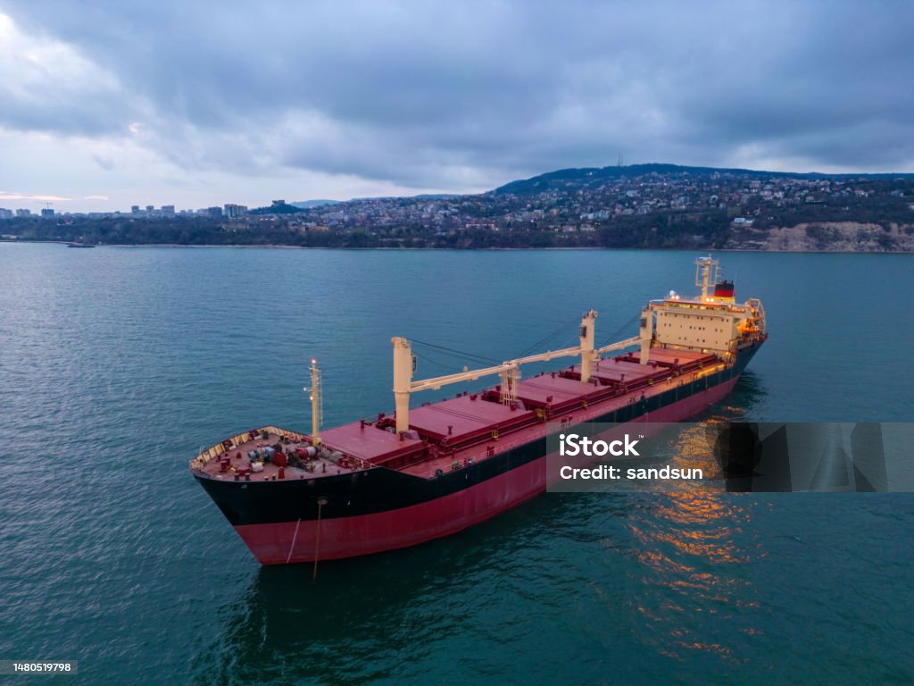 aerial view of a bulk carrier at evening showcases a stunning display of lights reflecting off the water as the massive vessel cuts through the waves. aerial view of a bulk carrier at evening showcases a stunning display of lights reflecting off the water as the massive vessel cuts through the waves. The contrast between the darkness of the ocean and the brightly lit ship creates a captivating and atmospheric scene. Bulk Carrier Stock Photo