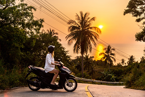 Woman tourist on a scooter during amazing sunet on a thailand island