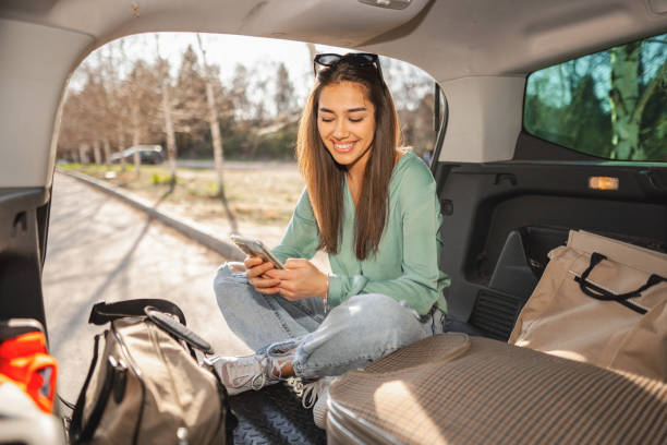 istock Young woman sitting in a car trunk using phone 1480520678