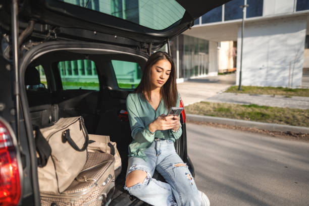 istock Young woman sitting in a car trunk using phone 1480520682