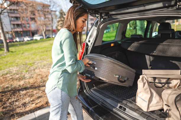 istock Young woman pulling luggage out of car trunk 1480520699