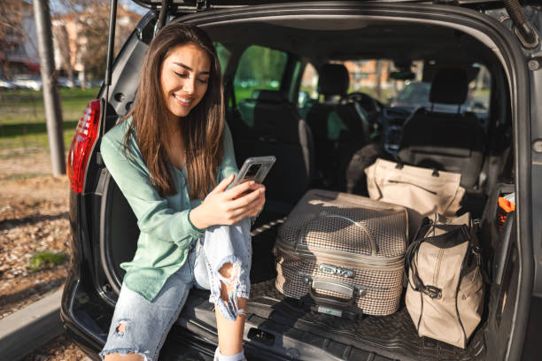 istock Young woman sitting in a car trunk using phone 1480520762