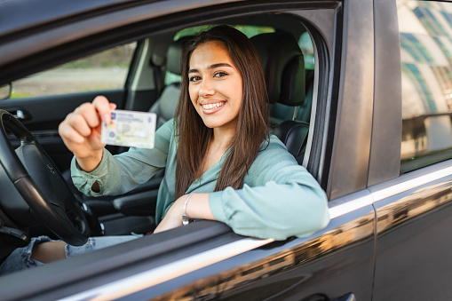 Portrait of a smiling young woman sitting in the drivers seat holding drivers license