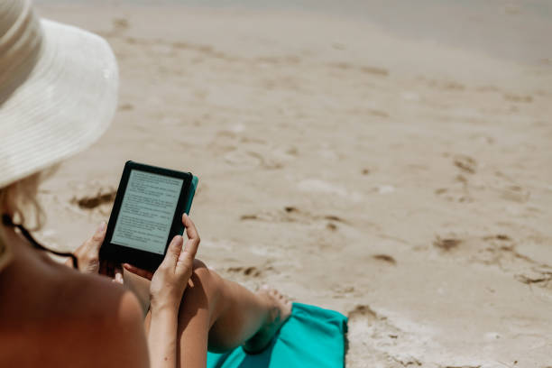 istock Woman relaxes while reading a book on her ereader on the beach 1480533464