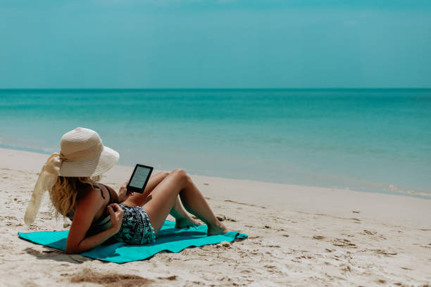 istock Woman relaxes while reading a book on her ereader on the beach 1480544875