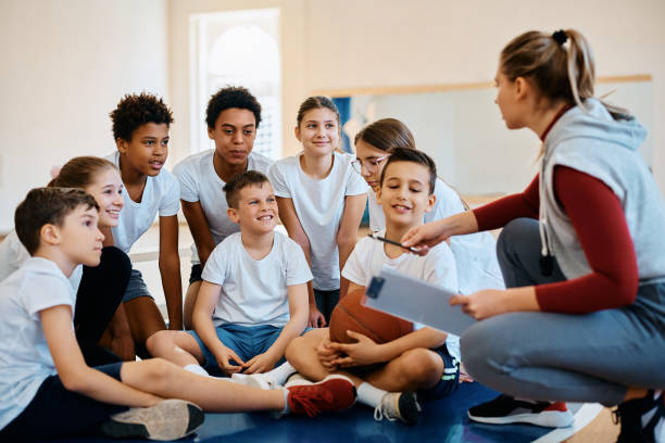 istock Happy elementary students listening their basketball coach during physical education class at school gym. 1480546980
