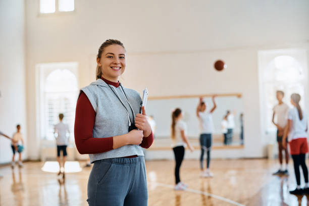 Young happy female coach during PE class at elementary school gym looking at camera.