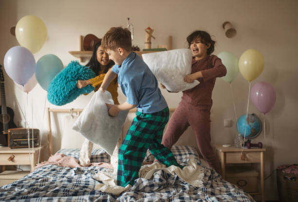 tres amigos felices divirtiéndose con almohadas en una cama. - lucha con almohada fotografías e imágenes de stock