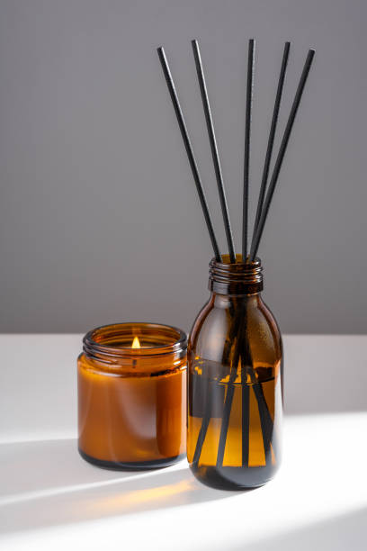 istock Aroma diffuser with natural essential oil in brown glass refill packaging bottle, soy wax candle with fire in a Amber jar on a white gray background. Concept mental health, calming and harmony 1480547222