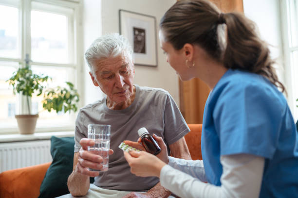 Nurse giving pills senior man in his home. stock photo