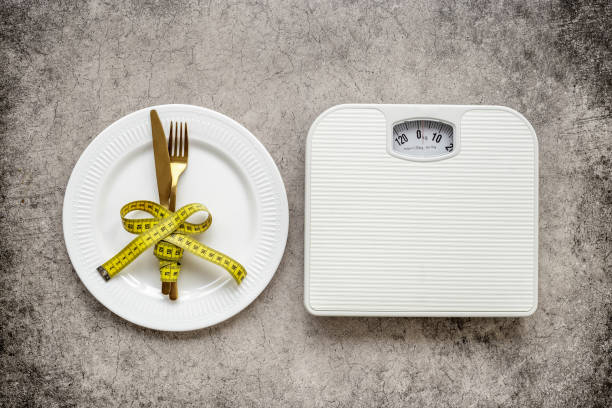 istock Weight scale and tape measure over dinner fork and knife on the plate 1480549773