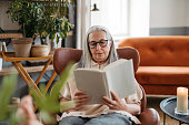 Senior woman reading book, enjoying time alone in her apartment.