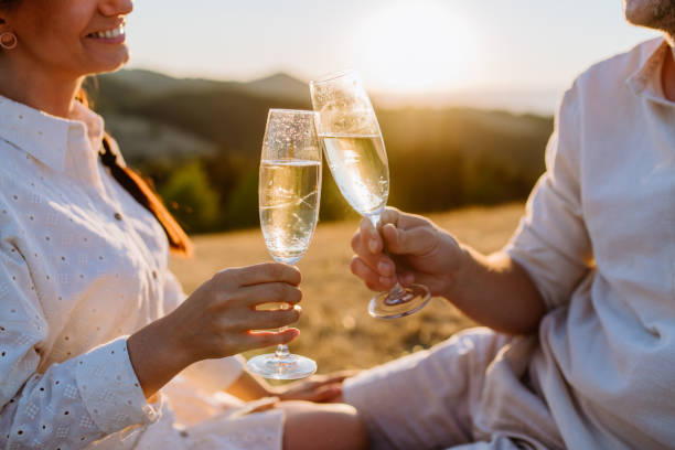 Close up of couple in love enjoying picnic and drinking wine on the hill at sunset. stock photo