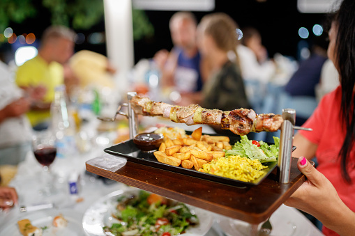 Dinner party in summer, special serving of grilled meat and vegetables on skewer with fries and salads