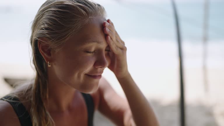 Blonde caucasian female surfer applying sunscreen on her face. Tanned young surfing woman putting spf on her cheeks, nose and forehead close-up. Portrait of surfer girl usinf spf skin protection