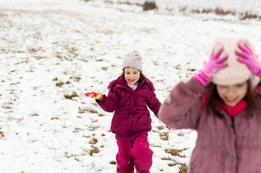 Two happy girls playing at the snow on the meadow during winter day