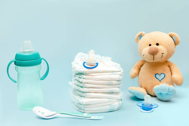 istock Stack of diapers with cute teddy bear toy, bottle milk, pacifier, spoons on table. set for infant newborn boy girl for baby shower present gift on blue background. Healthcare medical, hygiene concept 1480557449