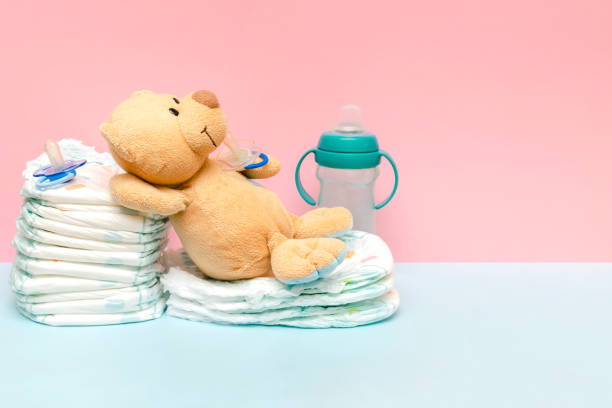 Stack of diapers with cute teddy bear toy pacifier lying on table. set for infant newborn boy girl for baby shower present gift on blue pink background copy space. Healthcare medical, hygiene concept Stack of diapers with cute teddy bear toy pacifier lying on table. set for infant newborn boy girl for baby shower present gift on blue pink background copy space. Healthcare medical, hygiene concept. pink teddy bear stock pictures, royalty-free photos & images