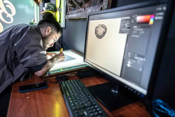 Photo of Young man drawing on a paper at tattoo studio