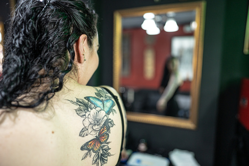 Woman looking on the mirror the tattoo on her back at tattoo studio