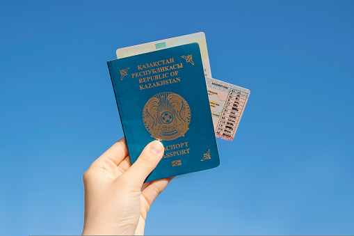 Hand holds the national passport of the Republic of Kazakhstan against the blue sky background. The national identity card kz and driver's license are in the passport. High quality photo.
