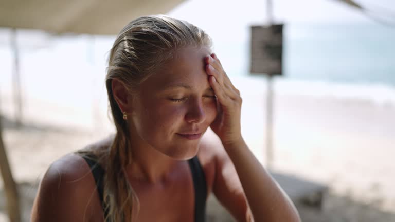 Blonde caucasian female surfer applying sunscreen on her face. Tanned young surfing woman putting spf on her cheeks, nose and forehead close-up. Portrait of surfer girl usinf spf skin protection