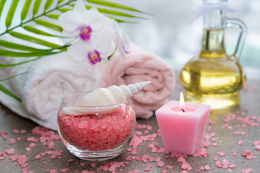 Spa composition with towels, red sea star, pink salt, oil bottle and green fern branch on stone background with free space for text