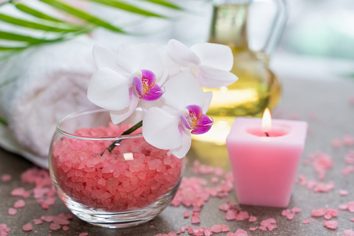 Spa composition with towels, red sea star, pink salt, oil bottle and green fern branch on stone background with free space for text