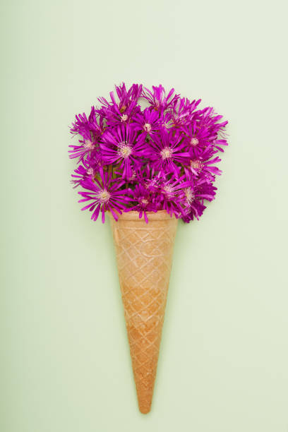Fresh wildflowers in ice cream cone on green background flat lay