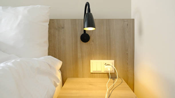istock Close-up fragment of bedroom with empty bedside table, turn on reading lamp and a socket in modern interior​ design home or hotel. Soft pillow and blanket, stylish comfortable furniture. 1480570227