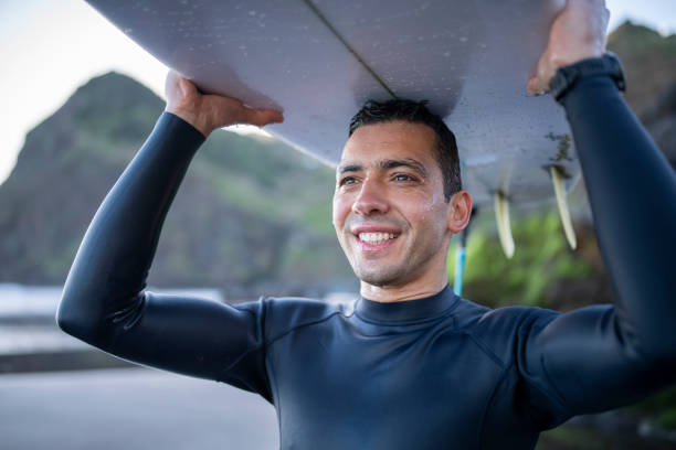 Portrait of smiling surfer lookinga at the ocean and carrying his board.