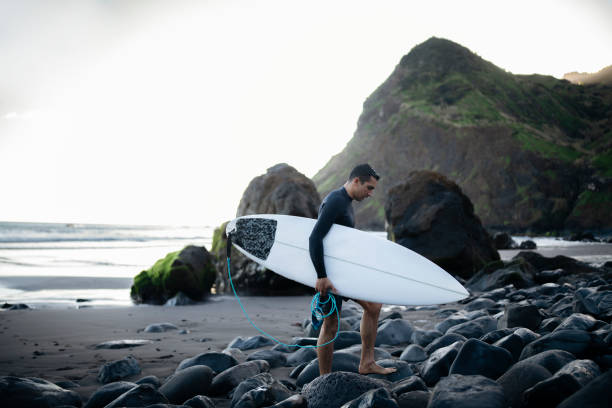 Man walking on the beautiful beach by the ocean and holding his surfboard.
