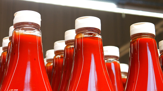 Many beautiful bottles of ketchup on a supermarket  shelf close-up