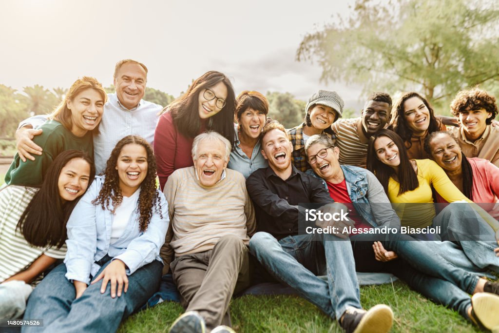 Happy multigenerational people having fun sitting on grass in a public park People Stock Photo