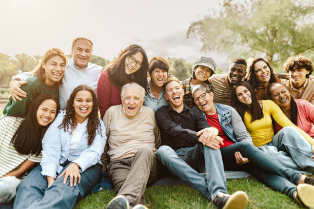 Happy multigenerational people having fun sitting on grass in a public park stock photo