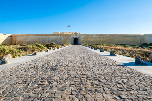 grande ingresso della maestosa fortezza fortaleza de sagres in mostra in uno scatto grandangolare, con un vasto vialetto che conduce al cancello gigante e un imponente muro sotto il cielo blu di sagres, in portogallo. - sagres foto e immagini stock