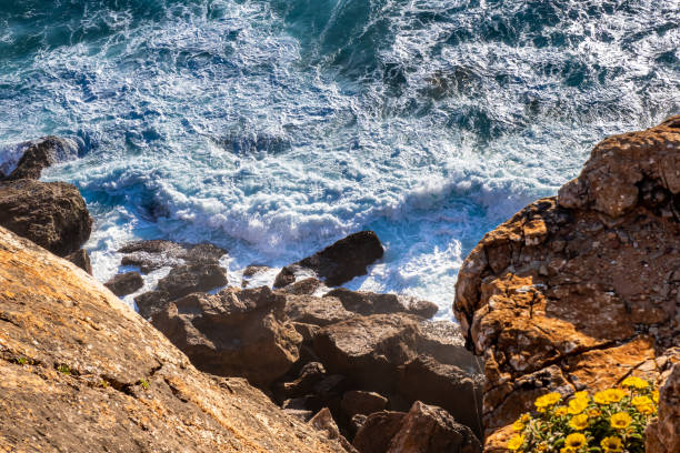 uma vista de parar o coração revela o poder de risco de vida do oceano atlântico à medida que as ondas batem violentamente contra rochas escarpadas, criando correntes perigosas na costa do algarve, em portugal. - rugged coastline - fotografias e filmes do acervo