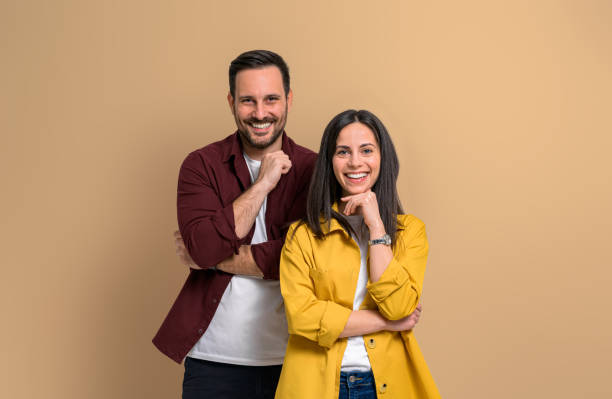 istock Charming young man and woman with hands on chins smiling and looking at camera. Confident joyful boyfriend and girlfriend wearing casuals and posing over beige background 1480586556