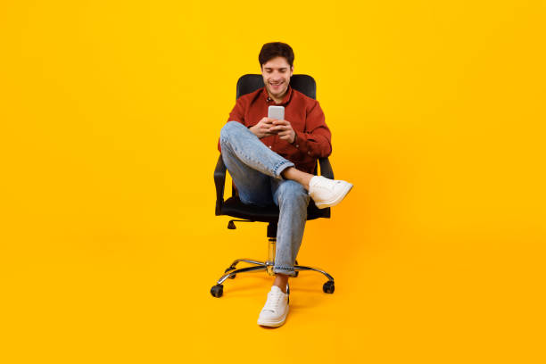 istock Happy Man Using Phone Texting Sitting In Chair, Yellow Background 1480589768