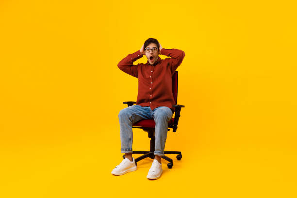 istock Shocked Man Touching Head Sitting Looking At Camera, Yellow Background 1480589772