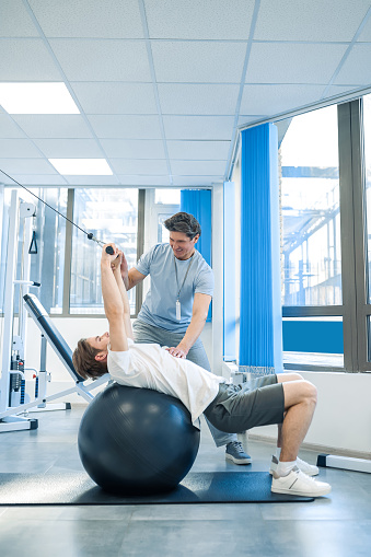 Rehabilitation exercises. Male patient having a session of rehabilitation exercises on a fitball