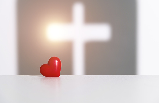 Religious cross shadow and red heart on white background