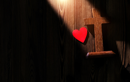 Religious cross and red heart on wooden table