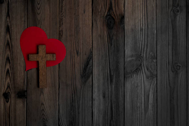 Religious cross and red heart on wooden table