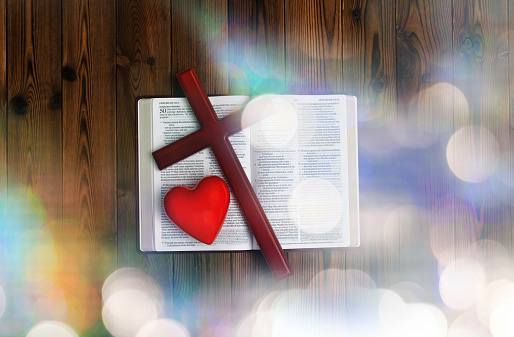 Bible, religious cross and red heart on wooden table