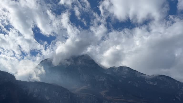 Low-hanging clouds stretch through powerful mountains against a cloudy blue sky