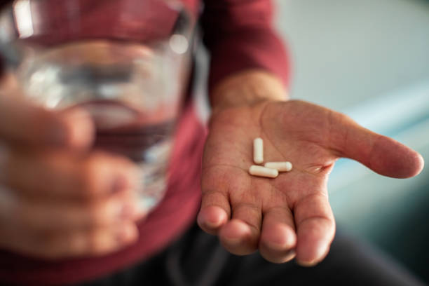 senior man taking a pill in a bathroom - bottle vitamin pill nutritional supplement white imagens e fotografias de stock