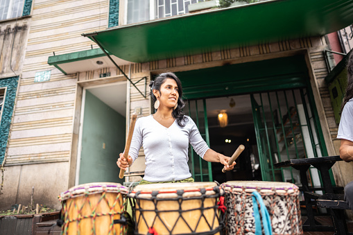 Mid adult woman playing djembe drum using a drumstick outdoors